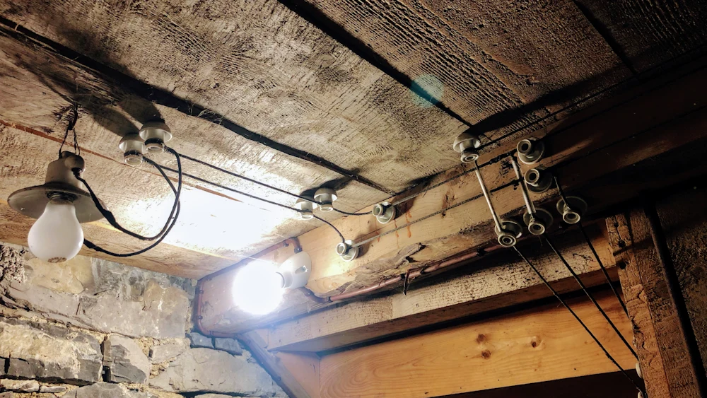 Old exposed wiring and bare bulbs in an unfinished basement ceiling.