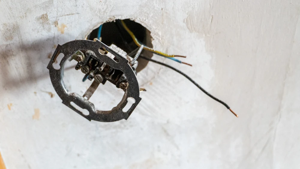 Exposed wires hanging from an open junction box in a ceiling.
