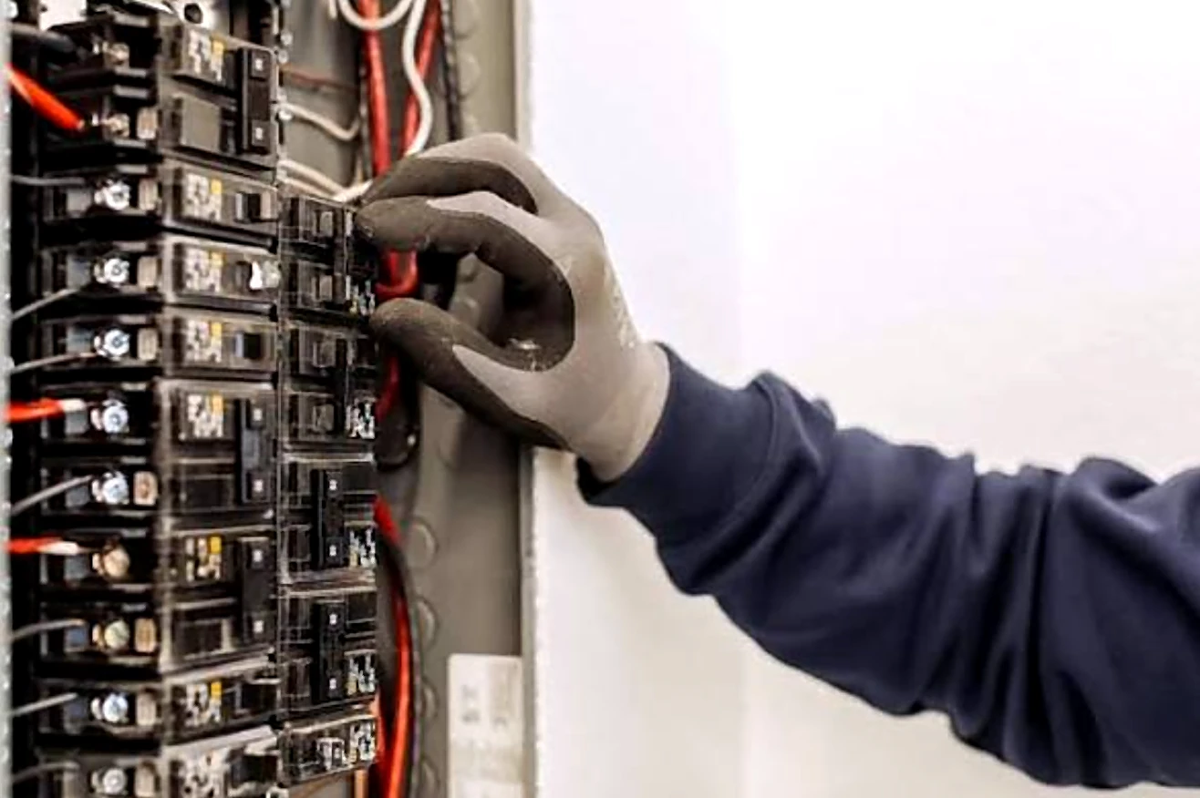 A gloved hand working on breakers in a residential electrical panel.