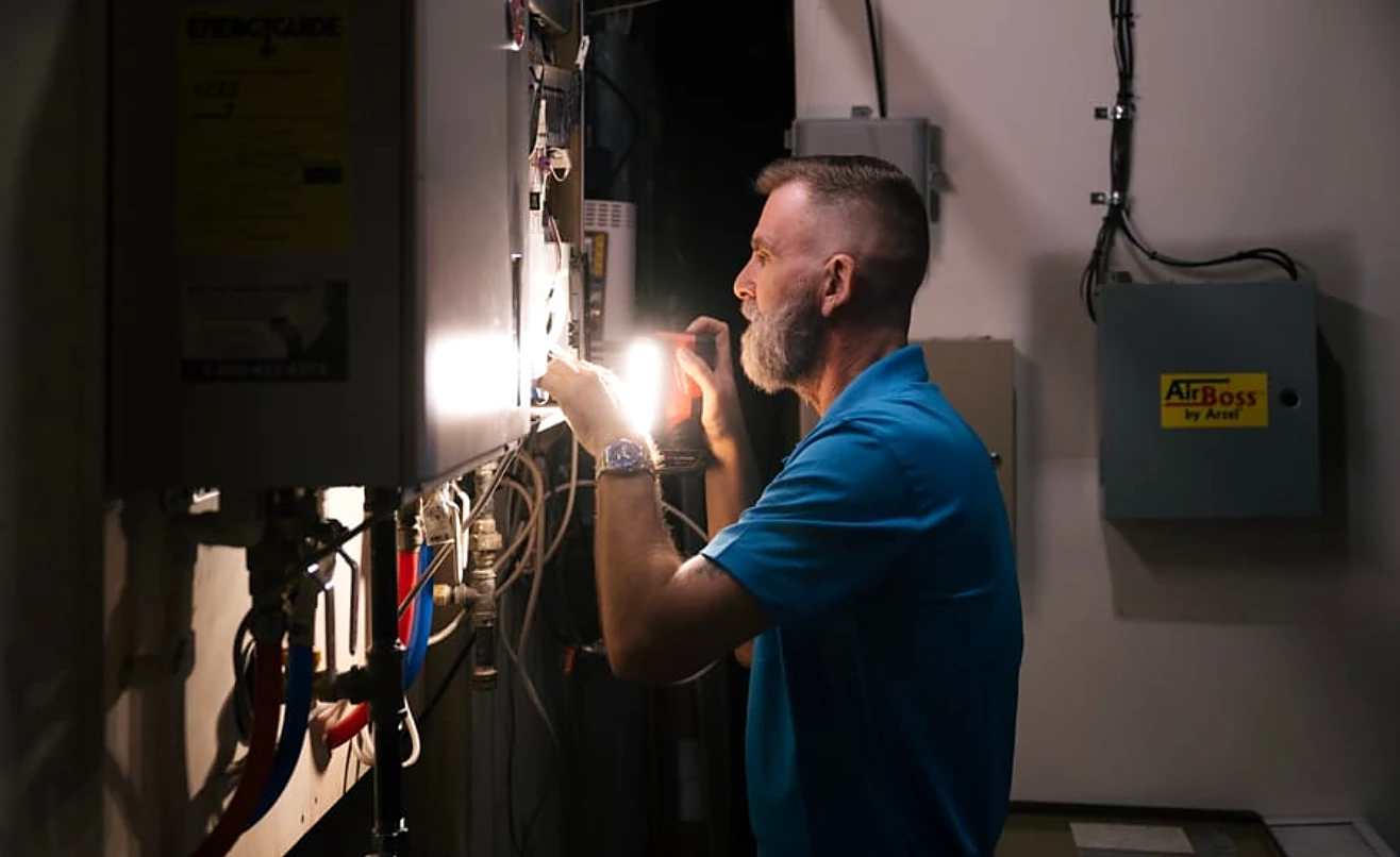 An electrician tracing wiring in an open panel with a flashlight.